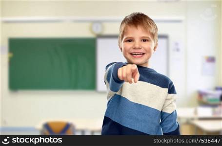 school, education and gesture concept - portrait of smiling little boy in striped pullover pointing finger over classroom background. little boy pointing finger at school
