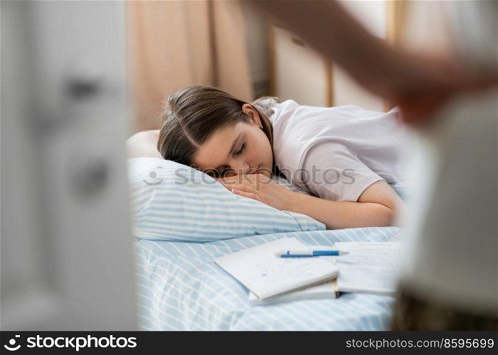 school, education and laziness concept - close up of angry parent looking at tired teenage student girl with notebooks sleeping on bed at home. parent looking at student girl sleeping at home
