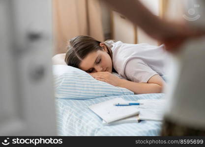 school, education and laziness concept - close up of angry parent looking at tired teenage student girl with notebooks sleeping on bed at home. parent looking at student girl sleeping at home