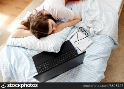 school, education and laziness concept - tired teenage student girl with laptop computer and notebooks sleeping on bed at home. tired student girl with laptop sleeping at home