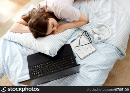 school, education and laziness concept - tired teenage student girl with laptop computer and notebooks sleeping on bed at home. tired student girl with laptop sleeping at home