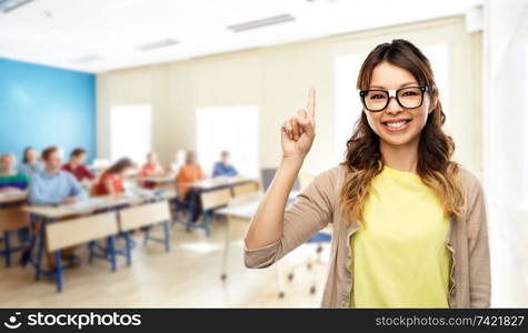 school, education and learning concept - happy asian woman or student in glasses fixed by tape pointing finger up over classroom background. asian woman or student with finger up at school