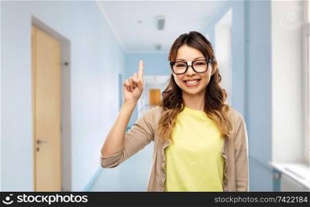 school, education and learning concept - happy asian woman or student in glasses fixed by tape pointing finger up over corridor background. asian woman or student with finger up at school