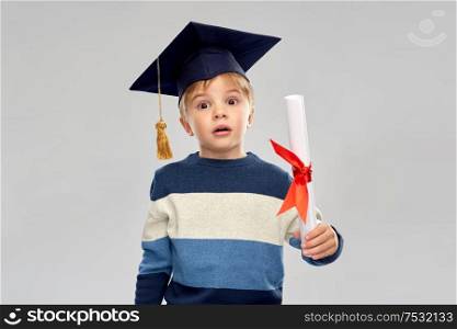 school, education and learning concept - happy little boy in bachelor hat or mortarboard with diploma over grey background. little boy in mortarboard with diploma
