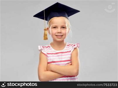 school, education and learning concept - happy little girl in bachelor hat or mortarboard over grey background. happy girl in bachelor hat or mortarboard