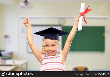 school, education and learning concept - happy little girl in bachelor hat or mortarboard with diploma celebrating success over classroom background. happy little girl in mortarboard with diploma