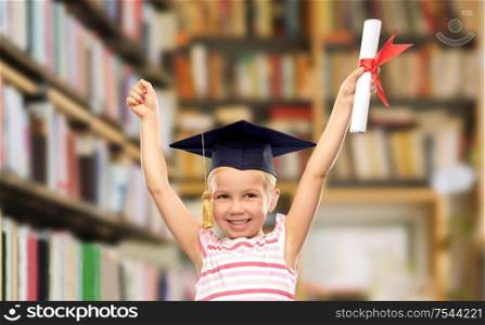 school, education and learning concept - happy little girl in bachelor hat or mortarboard with diploma celebrating success over library book shelves background. happy little girl in mortarboard with diploma
