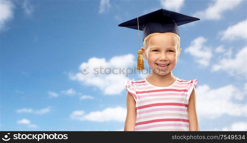 school, education and learning concept - happy little girl in bachelor hat or mortarboard over blue sky and clouds background. happy girl in bachelor hat or mortarboard