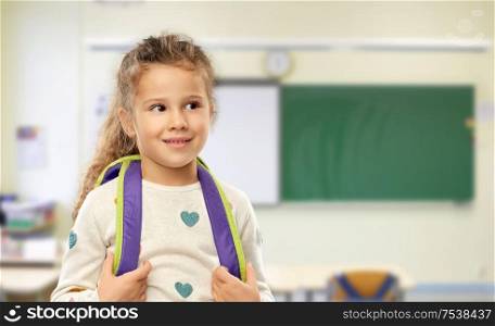 school, education and learning concept - happy little girl with backpack over classroom background. happy little girl with backpack at school