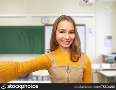 school, education and learning concept - happy smiling young teenage student girl taking selfie over classroom background. happy student girl taking selfie at school