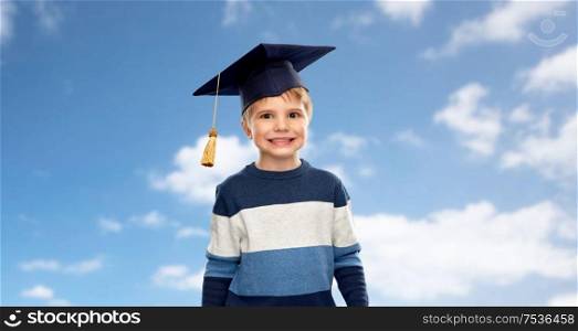 school, education and learning concept - little boy in bachelor hat or mortarboard over blue sky and clouds background. little boy in bachelor hat or mortarboard over sky