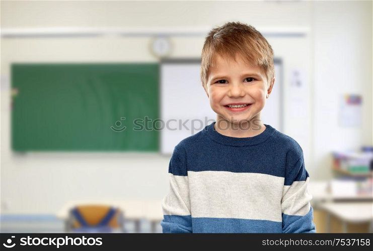 school, education and learning concept - portrait of nice little boy in striped pullover over classroom background. happy smiling little boy at school