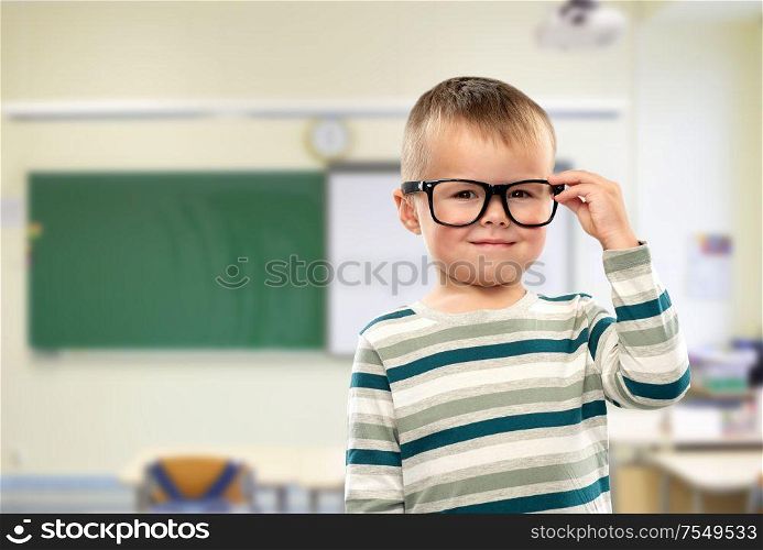 school, education and learning concept - portrait of smiling little boy in glasses over classroom background. portrait of smiling boy in glasses at school