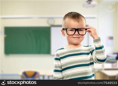 school, education and learning concept - portrait of smiling little boy in glasses over classroom background. portrait of smiling boy in glasses at school