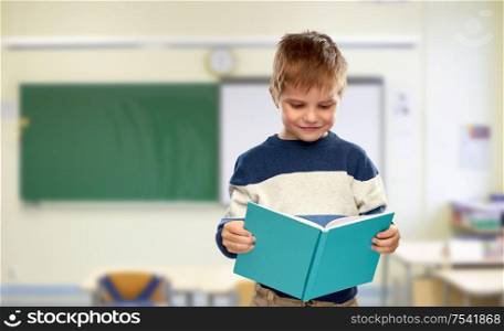school, education and learning concept - smiling little boy reading book over classroom background. smiling little boy reading book at school