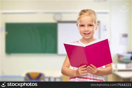 school, education and learning concept - smiling little girl reading book over classroom background. smiling little girl reading book at school