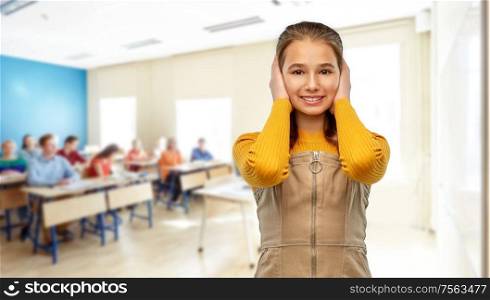 school, education and learning concept - smiling teenage student girl closing ears by hands over classroom background. student girl closing ears by hands at school