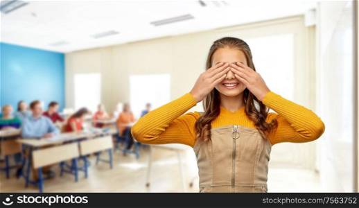 school, education and learning concept - smiling teenage student girl closing her eyes by hands over classroom background. smiling student girl closing her eyes by hands