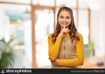 school, education and learning concept - young teenage girl making hush gesture over classroom background. young teenage girl making hush gesture at school