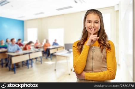 school, education and learning concept - young teenage student girl making hush gesture over classroom background. student girl making hush gesture at school