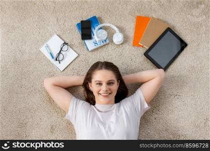 school, education and people concept - happy smiling student girl with books and gadgets lying on floor at home. happy student girl with books and gadgets on floor