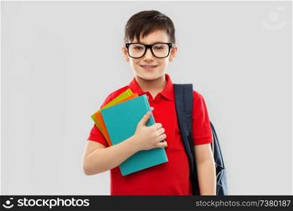 school, education and people concept - portrait of smiling little student boy in red polo t-shirt in glasses with books and bag over grey background. smiling schoolboy in glasses with books and bag