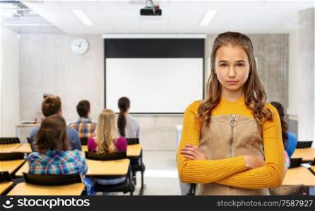 school, education and people concept - serious young teenage student girl with crossed arms over classroom background. serious student girl with crossed arms at school