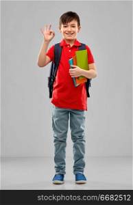 school, education and people concept - smiling little student boy in red polo t-shirt in glasses with books and bag showing ok hand sign over grey background. student boy with books and school bag showing ok