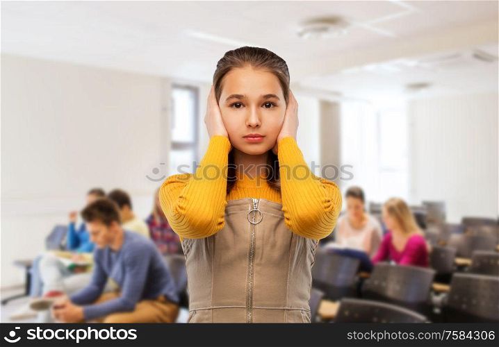 school, education and people concept - stressed teenage student girl closing ears by hands over lecture hall background. student girl closing ears by hands at school
