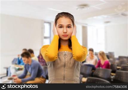school, education and people concept - stressed teenage student girl closing ears by hands over lecture hall background. student girl closing ears by hands at school