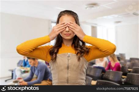 school, education and people concept - teenage student girl closing her eyes by hands over lecture hall background. student girl closing her eyes by hands at school