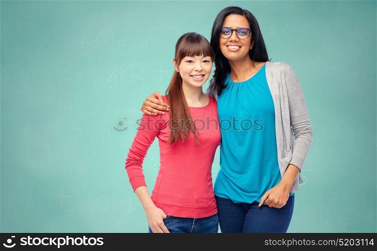 school, education and people concept - two happy smiling international women students over green chalk board background. international students over school chalk board