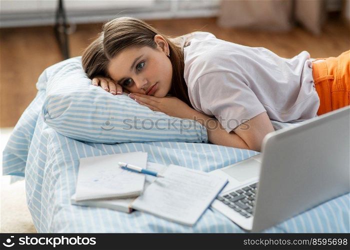 school, education and stress concept - tired teenage student girl with laptop computer and notebooks lying on bed at home. tired student girl with laptop lies on bed at home