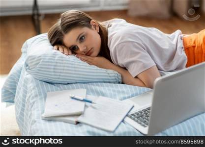 school, education and stress concept - tired teenage student girl with laptop computer and notebooks lying on bed at home. tired student girl with laptop lies on bed at home