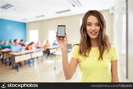 school, education and technology concept - smiling teenage student girl in yellow t-shirt holding smartphone with blank screen over classroom background. teenage student girl holding smartphone at school