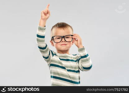 school, education and vision concept - portrait of smiling little boy in glasses pointing finger up over grey background. portrait of boy in glasses pointing finger up