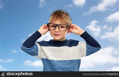 school, education and vision concept - portrait of smiling little boy in glasses over blue sky and clouds background. portrait of smiling little boy in glasses over sky