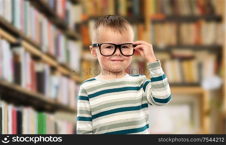 school, education and vision concept - portrait of smiling little boy in glasses over library background. portrait of smiling boy in glasses over library