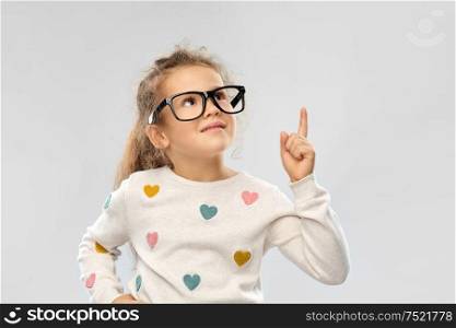 school, education and vision concept - portrait of smiling little girl in glasses pointing finger up over grey background. portrait of girl in glasses pointing finger up