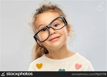 school, education and vision concept - portrait of smiling little girl in crookedly placed glasses over grey background. smiling little girl in crookedly placed glasses