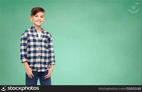 school, education, childhood and people concept - smiling student boy in checkered shirt and jeans over green school chalk board background