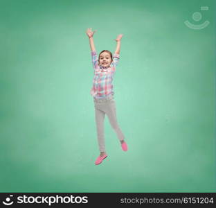 school, education, childhood, freedom and people concept - happy little girl jumping in air over green school chalk board background