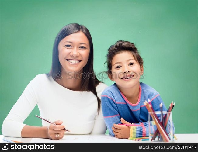 school, education, children and people concept - happy teacher and little schoolgirl drawing over green chalk board background