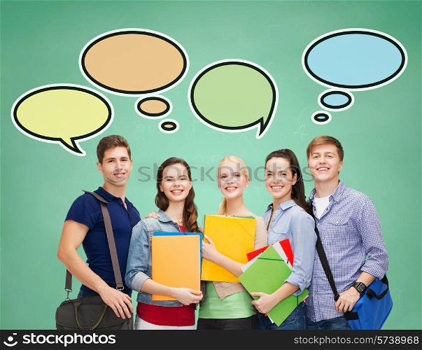 school, education, communication and people concept - group of smiling teenagers with folders and school bags over green board background with text bubbles