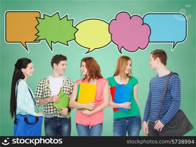 school, education, communication and people concept - group of smiling teenagers with folders and school bags talking over green board background with text bubbles