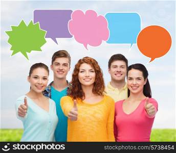 school, education, communication, gesture and people concept - group of smiling teenagers showing thumbs up over sky and grass with text bubbles