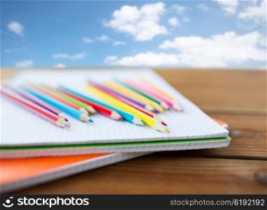 school, education, drawing and object concept - close up of crayons or color pencils on notebook paper over blue sky and clouds background