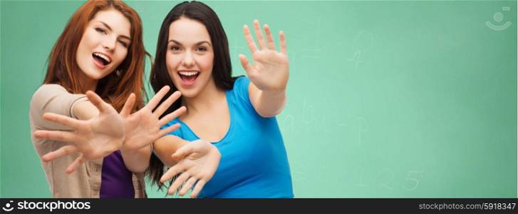 school, education, happiness and people concept - two smiling student girls or young women showing their palms over green chalk board background