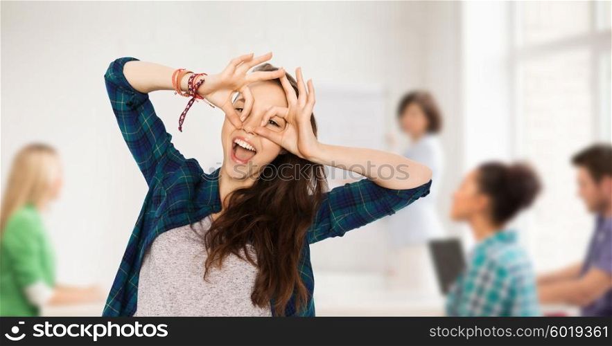 school, education, people and teens concept - happy smiling pretty teenage student girl making face and having fun over classroom background with teacher and classmates