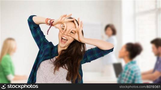 school, education, people and teens concept - happy smiling pretty teenage student girl making face and having fun over classroom background with teacher and classmates